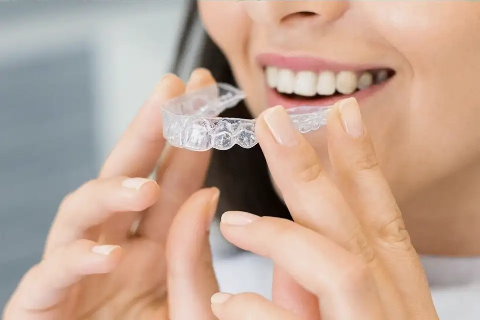 Close view of a hand holding a clear aligner tray near a smile