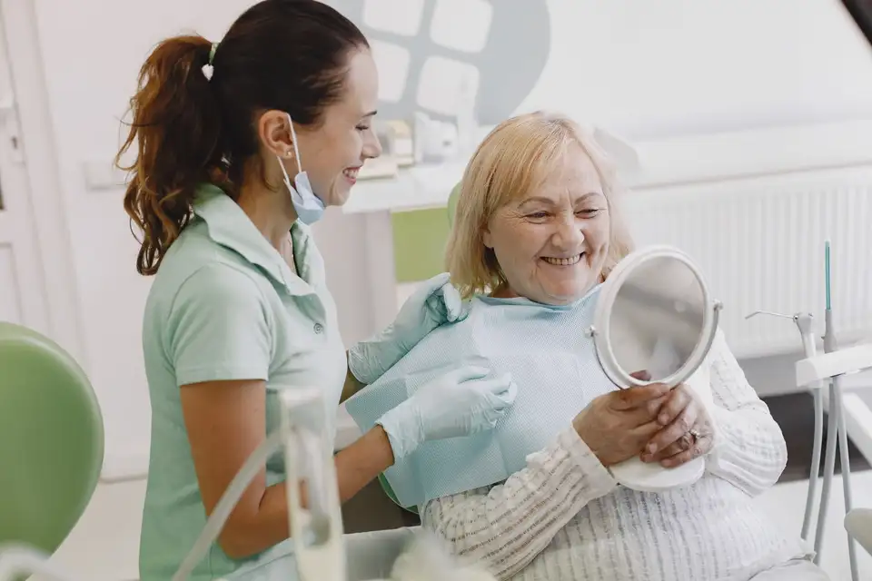 Older woman smiling at herself in a mirror held by her dentist
