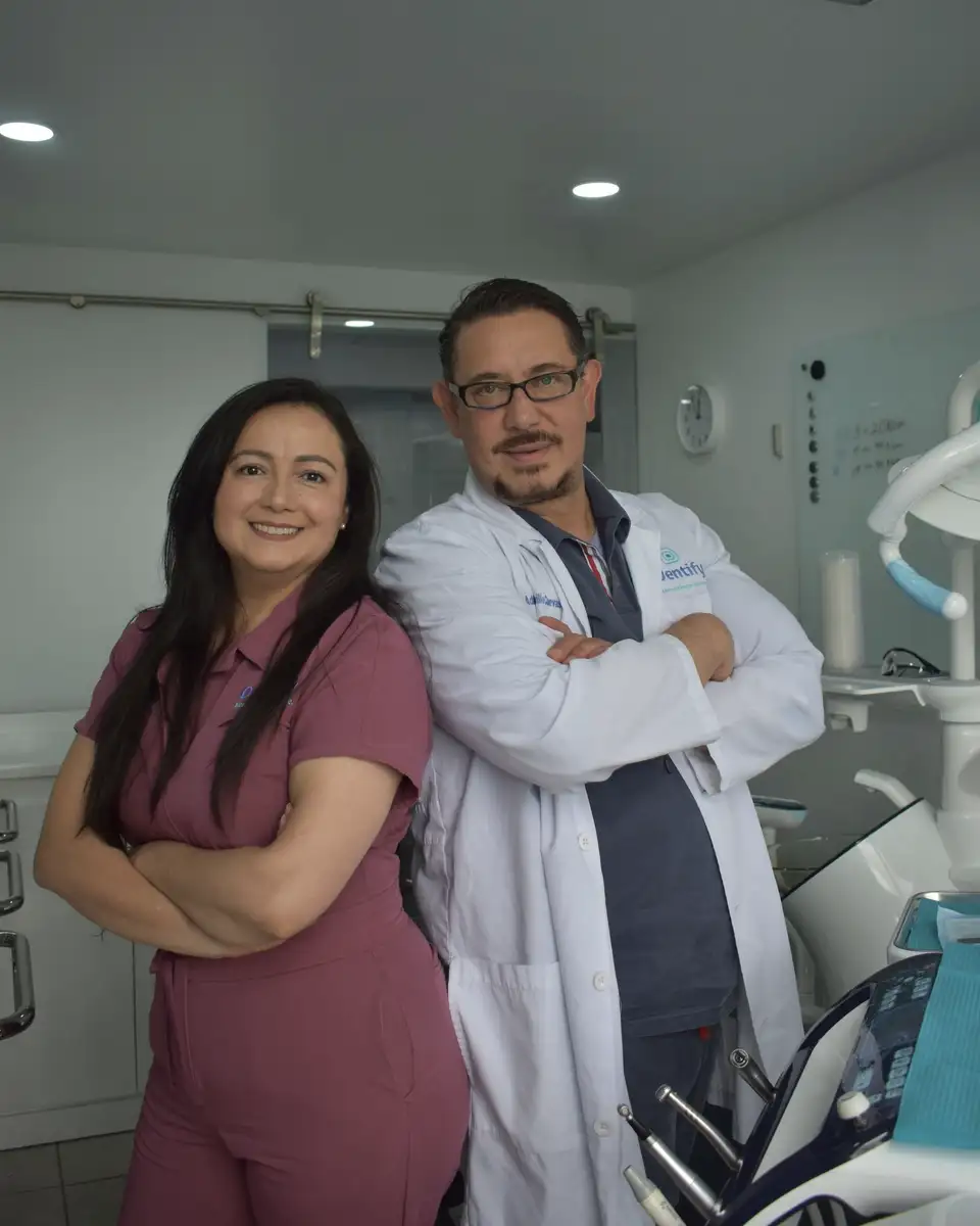 A dentist in a white coat and an assistant in scrubs in their treatment room