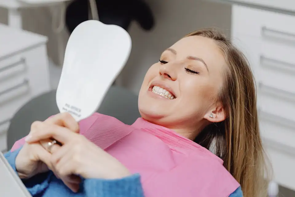 Woman in a dental chair smiling at herself in a hand mirror